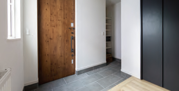 木製ドアとタイル貼りの床が見える玄関ホール。床面に埋め込まれた床暖房で、靴や傘立てなどがある温かみのあるエントランスの様子