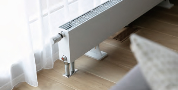 カーテン越しの窓際に設置されたパネルヒーター（セントラルヒーティング）の暖房装置。床下から循環する温水で室内を24時間暖める設備